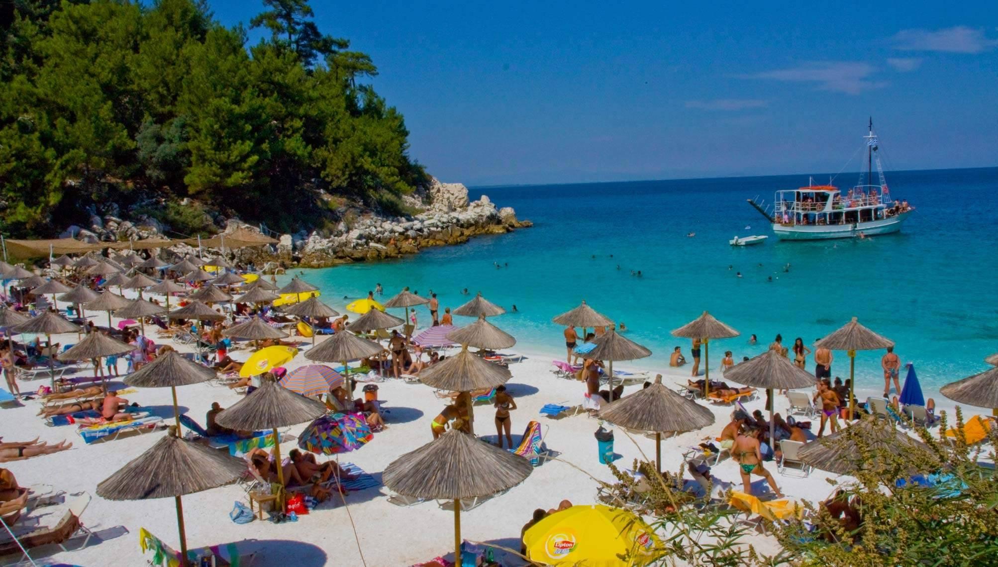 H Παραλία Σαλιάρα στη Θάσο πολλές ομπρέλες στην ακτή και ένα τουριστικό καραβάκι στη θάλασσα